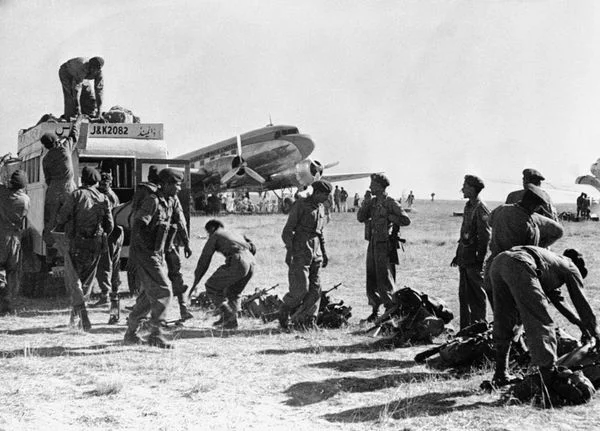 The initial days at Srinagar Airfield – a civilian bus embarks troops as a civilian Dakota in the background gets ready to take on civilian refugees for the return flight.